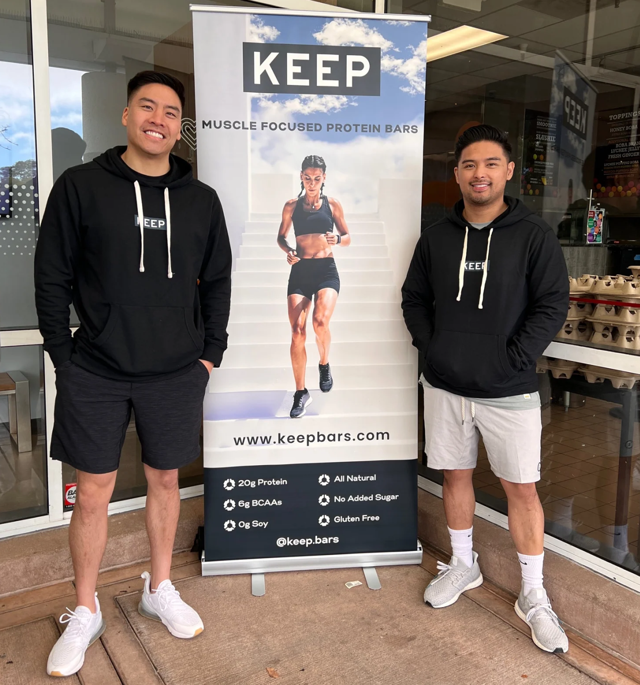 The owners of Keep Bars in front of a keep bar banner